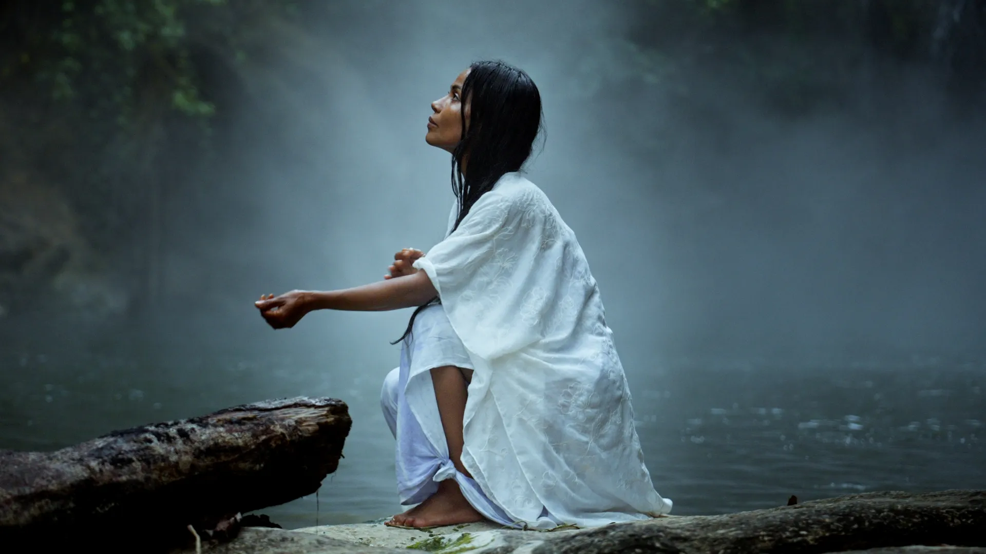 A still from Curandera: Tatiana kneeling by a misty waterfall